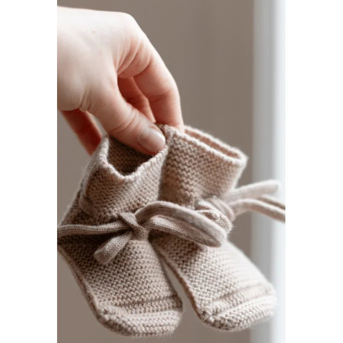Ein Paar gestrickte Babybooties mit Bindeschnürung in der Farbe Sand