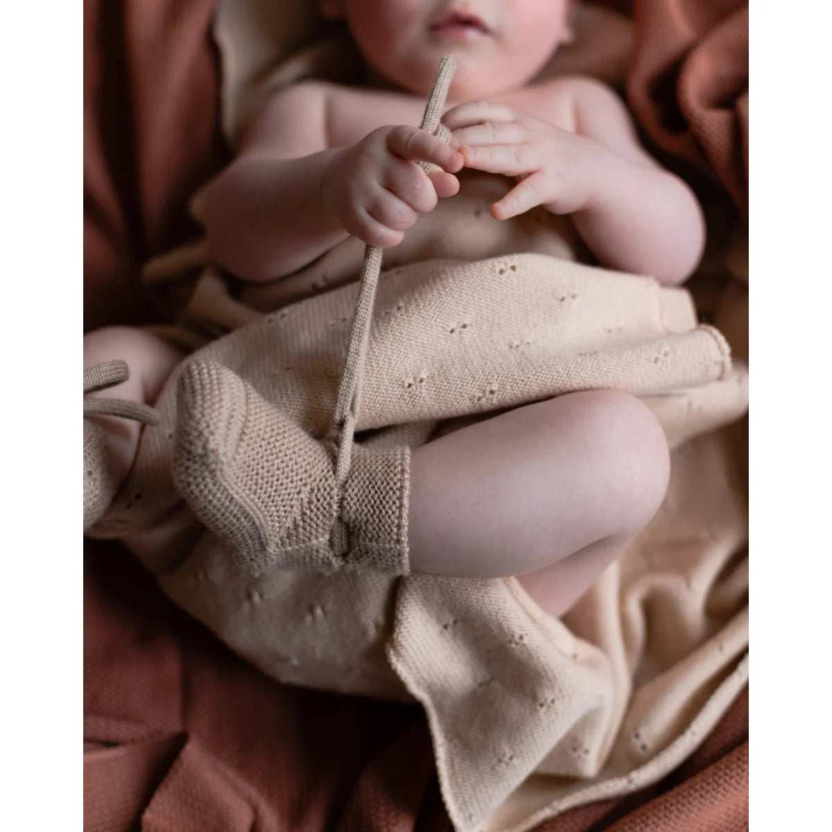 Baby mit gestrickten Sand-Booties hält einen Holzstock oder Spielzeug