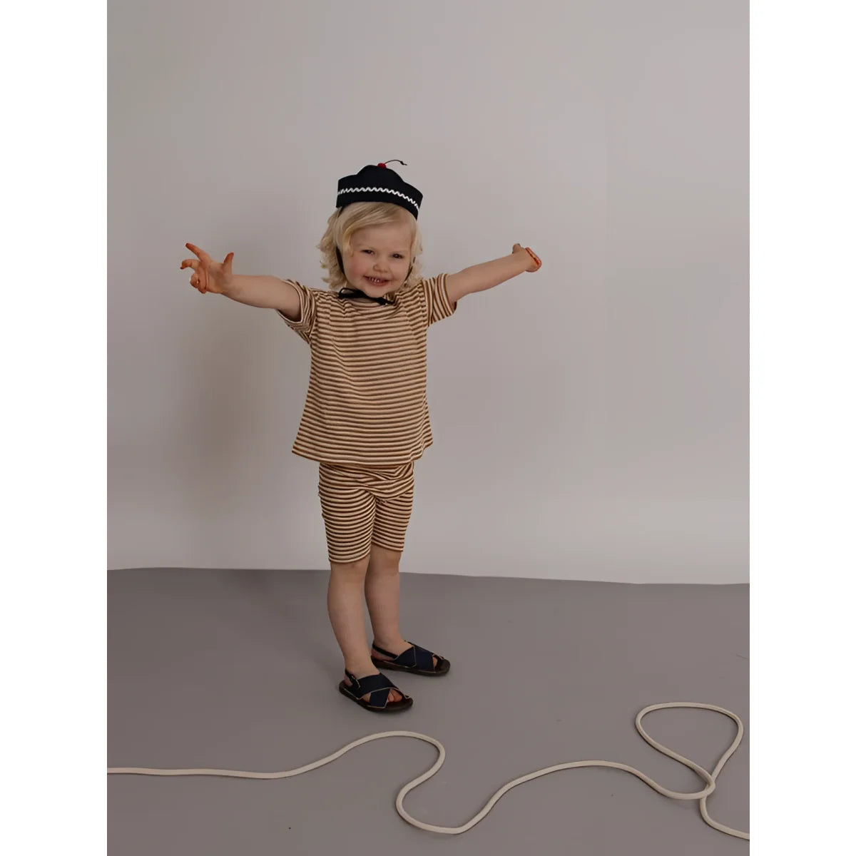 Kleinkind in Boxy T-Shirt Copper Stripes, beige-braun gestreift, mit Shorts, Sandalen und Baskenmütze
