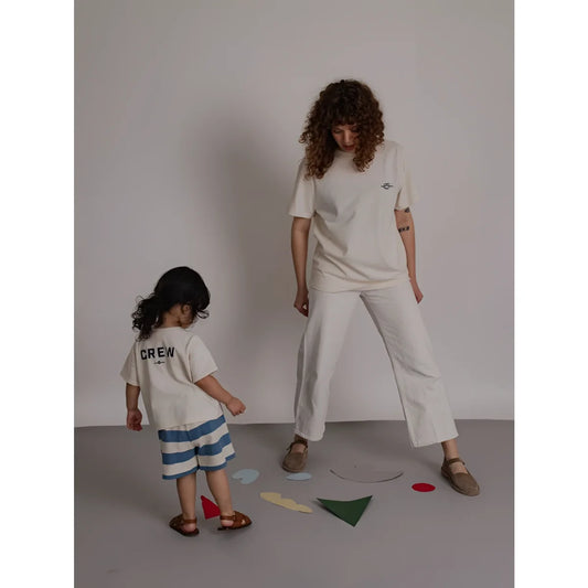 Eine frau trägt ein off white boxy t-shirt mit stickerei und weiten weißen hosen daneben steht ein kind in minimalistischer