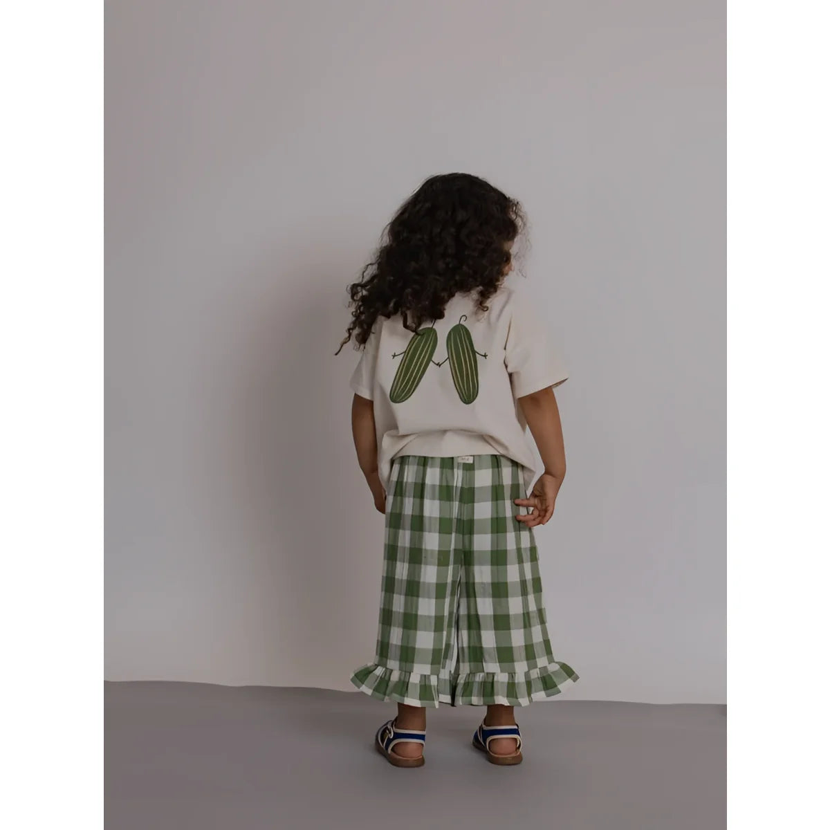 Rückseite: Kind in Boxy T-Shirt Friends Of the Garden mit Gurken-Print, Gingham-Hose