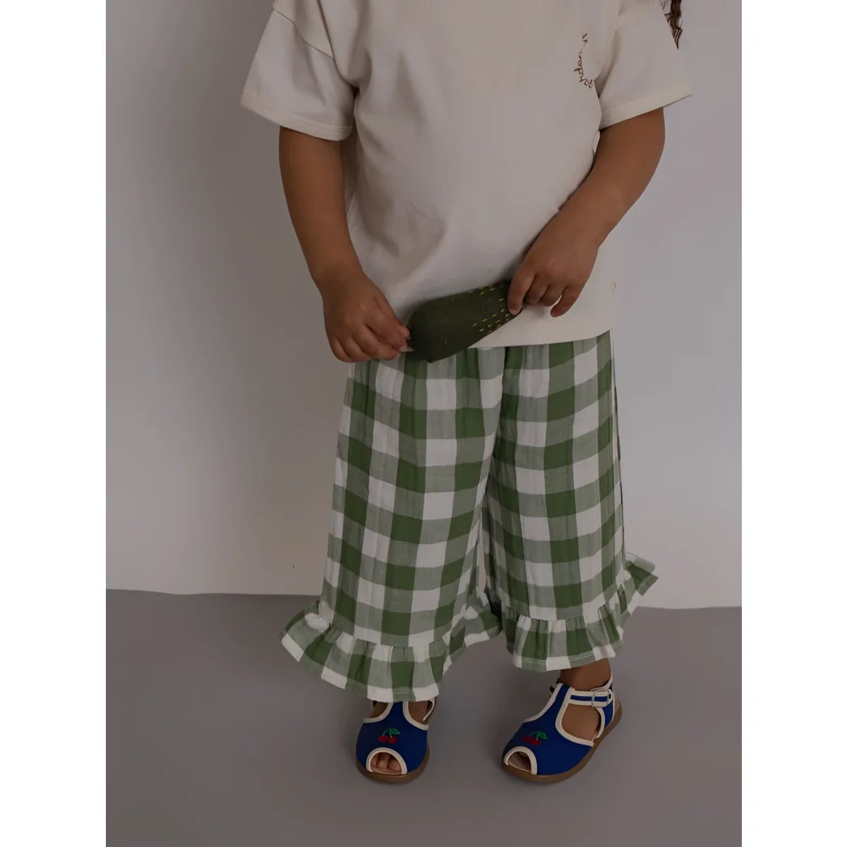 Kind trägt olivgrüne-weiße Karo Wide-Leg-Hose mit Rüschensaum zu Boxy T-Shirt Friends of the Garden