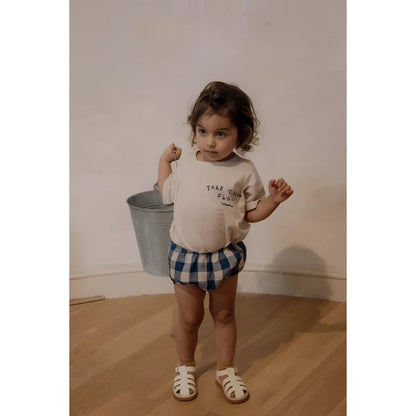 Junger Junge in cremefarbenem Shirt und Karoshorts mit Eimer in der Hand