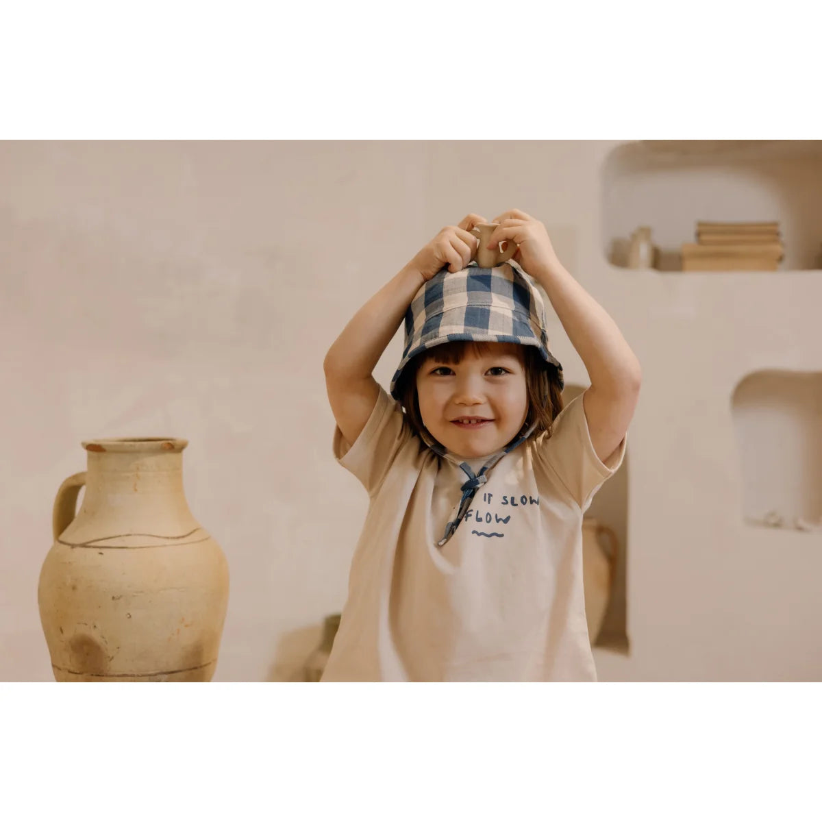 Lächelndes Kind mit karierter Bucket-Hat und beigem Shirt von Boxy T-shirt