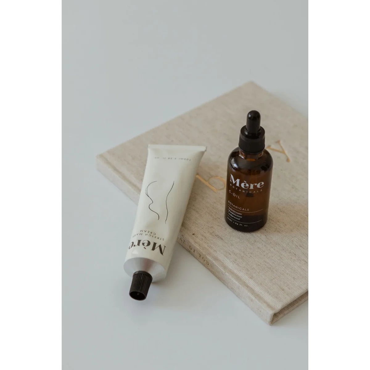 Skincare Produkte wie eine Tube und eine Glaspipette auf hellfarbener Stoffunterlage