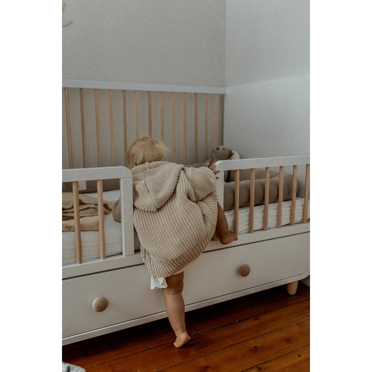 Weißes Holz-Kinderbett mit Kind, das in den Chunky Knit Cardigan | Oat klettert