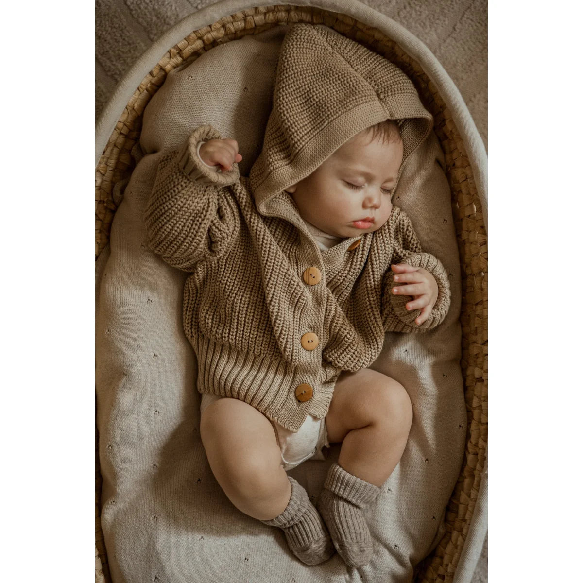 Schlafendes Baby in beigem Strickoutfit und Mütze in einem Korb