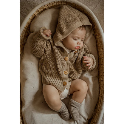 Schlafendes Baby in beigem Strickoutfit und Mütze in einem Korb