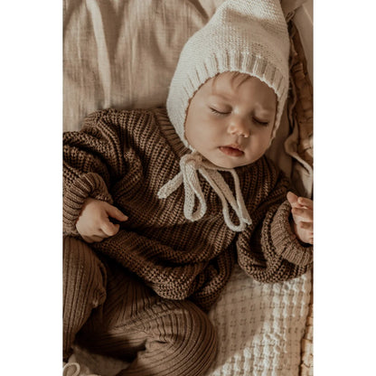 Schlafendes Baby in braunem Strickpullover und weißer Haube, Chunky Knit Sweater