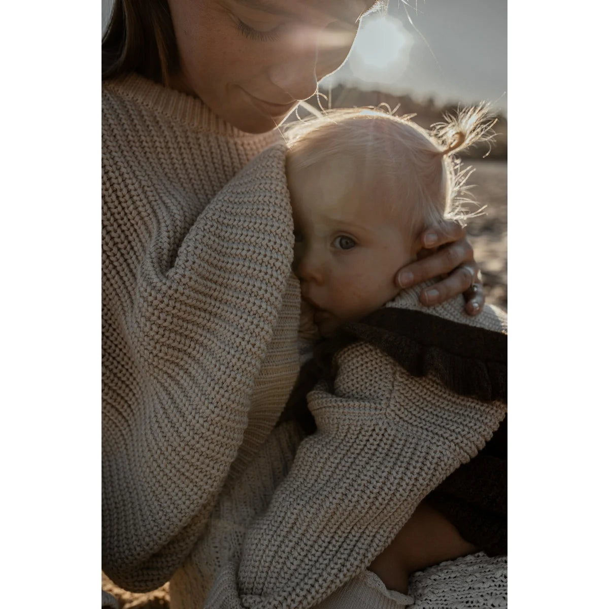 Eine Mutter umarmt ein Baby in einem Chunky Knit Sweater in Oat