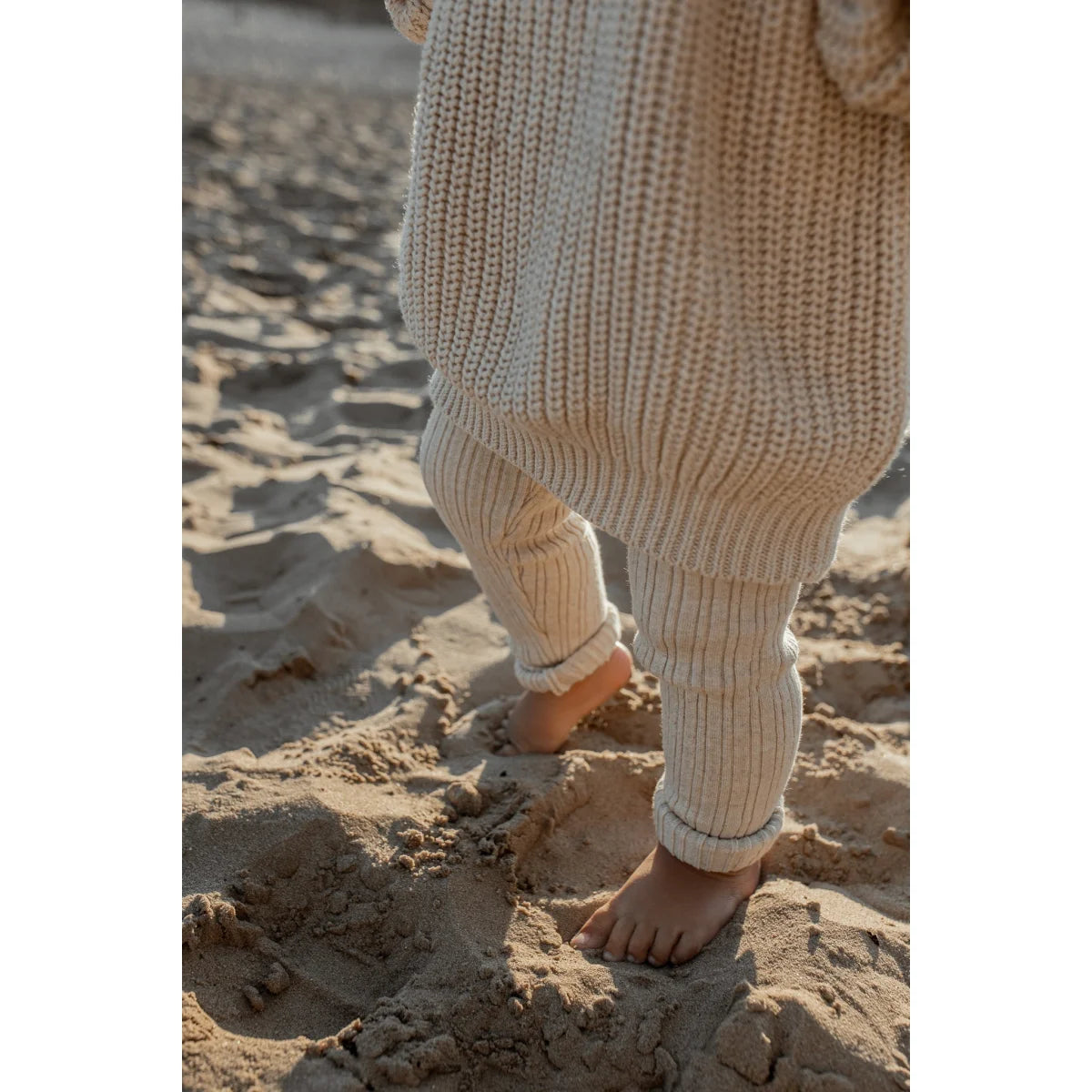 Barfuß im Sand mit lockeren, cremefarbigen Hosen und Chunky Knit Sweater in Haferfarbe