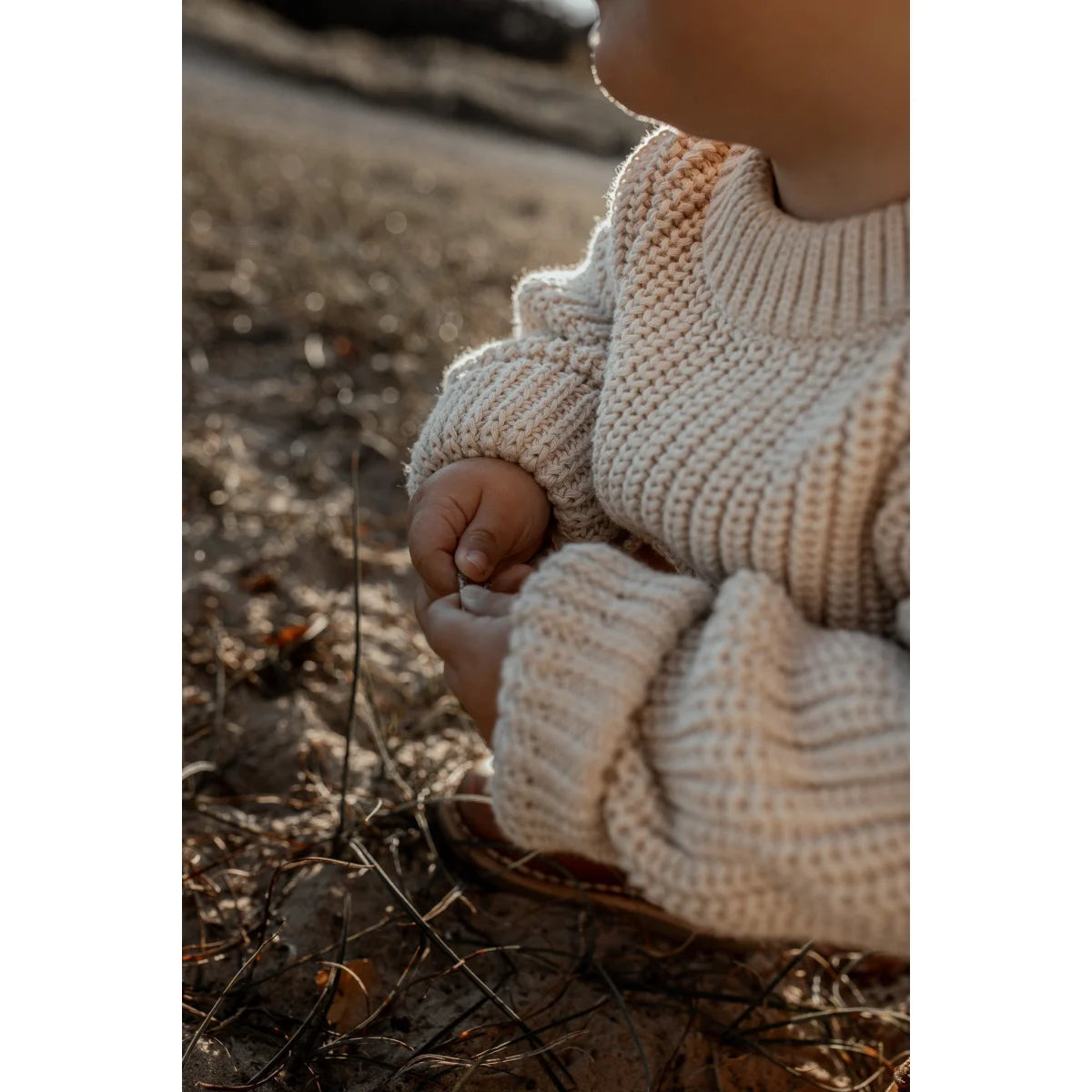 Kindliches Kind trägt cremigen, grob gestrickten Pullover auf dem Boden sitzend