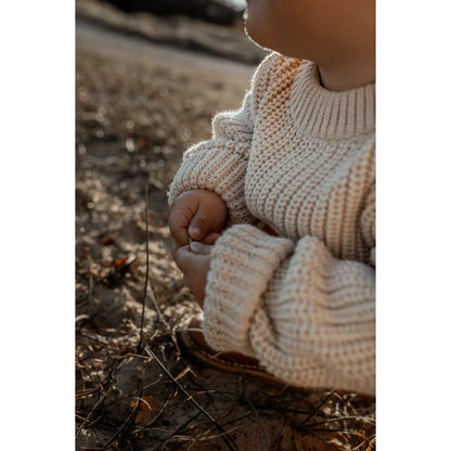 Kindliches Kind trägt cremigen, grob gestrickten Pullover auf dem Boden sitzend