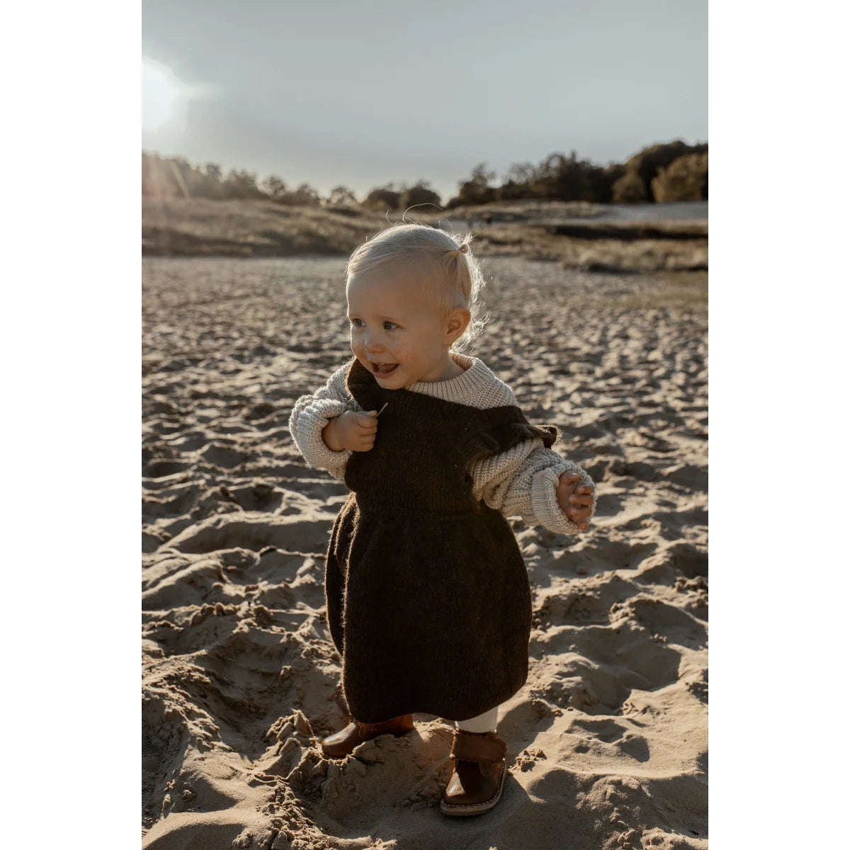 Lächelndes Baby in dunklem Outfit auf einem Sandstrand, Chunky Knit Sweater Oat