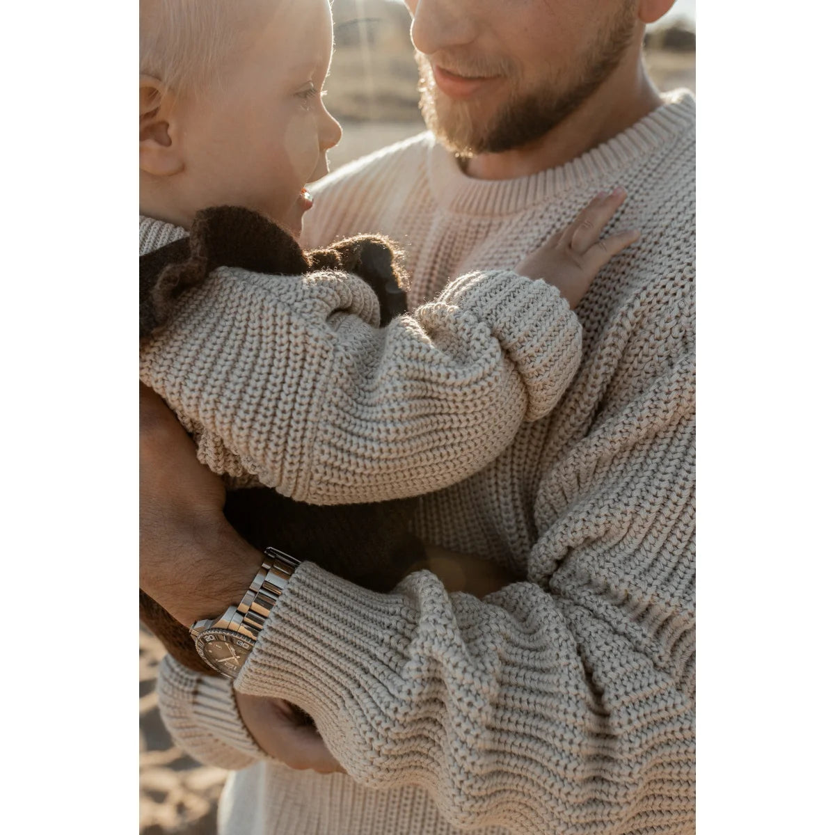 Erwachsener trägt einen Chunky Knit Sweater in Oat und hält ein Baby