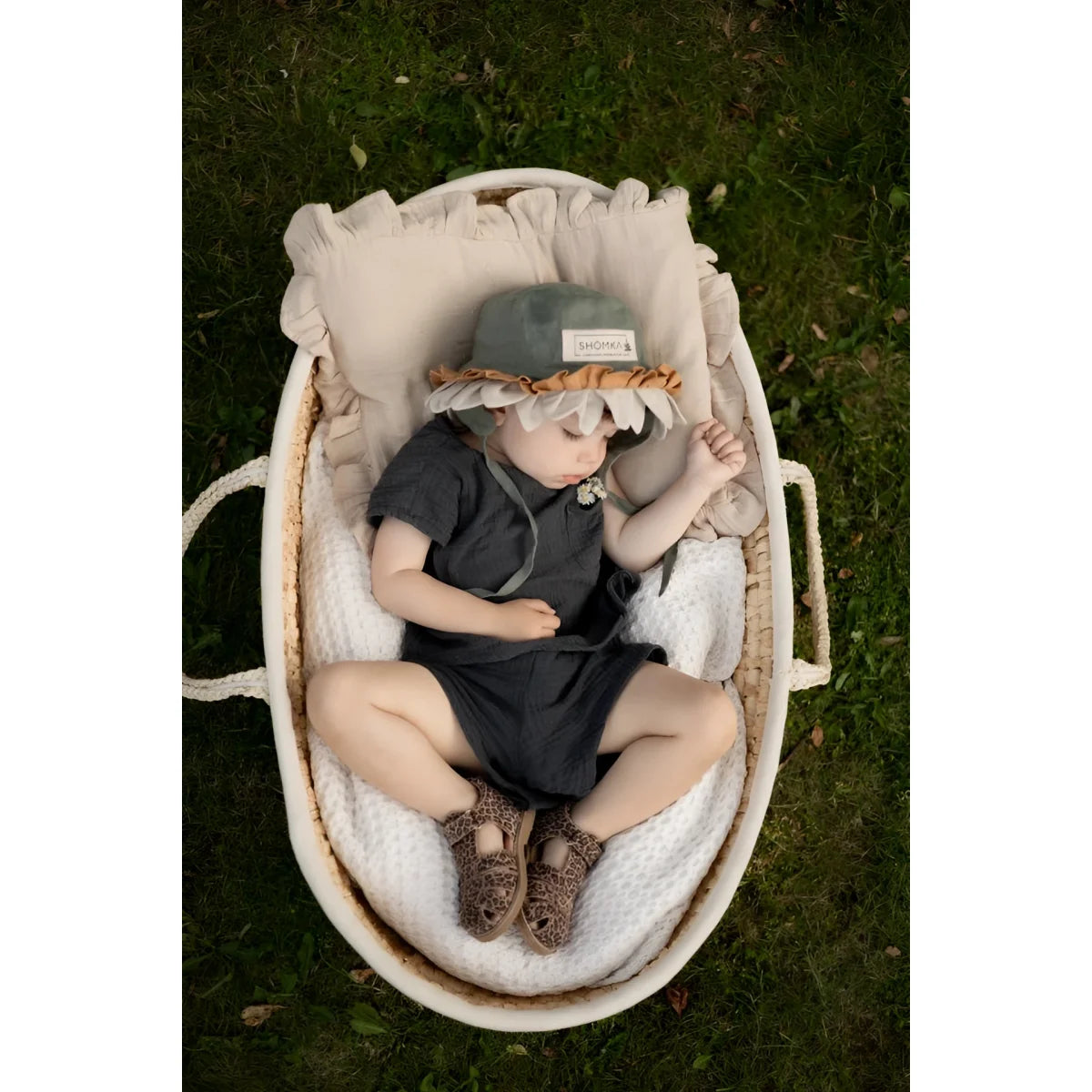 Ein baby trägt einen weichen grauen hut mit gerüschtem hellbraunem saum und sitzt in einem ovalen weidenkorb neben classic