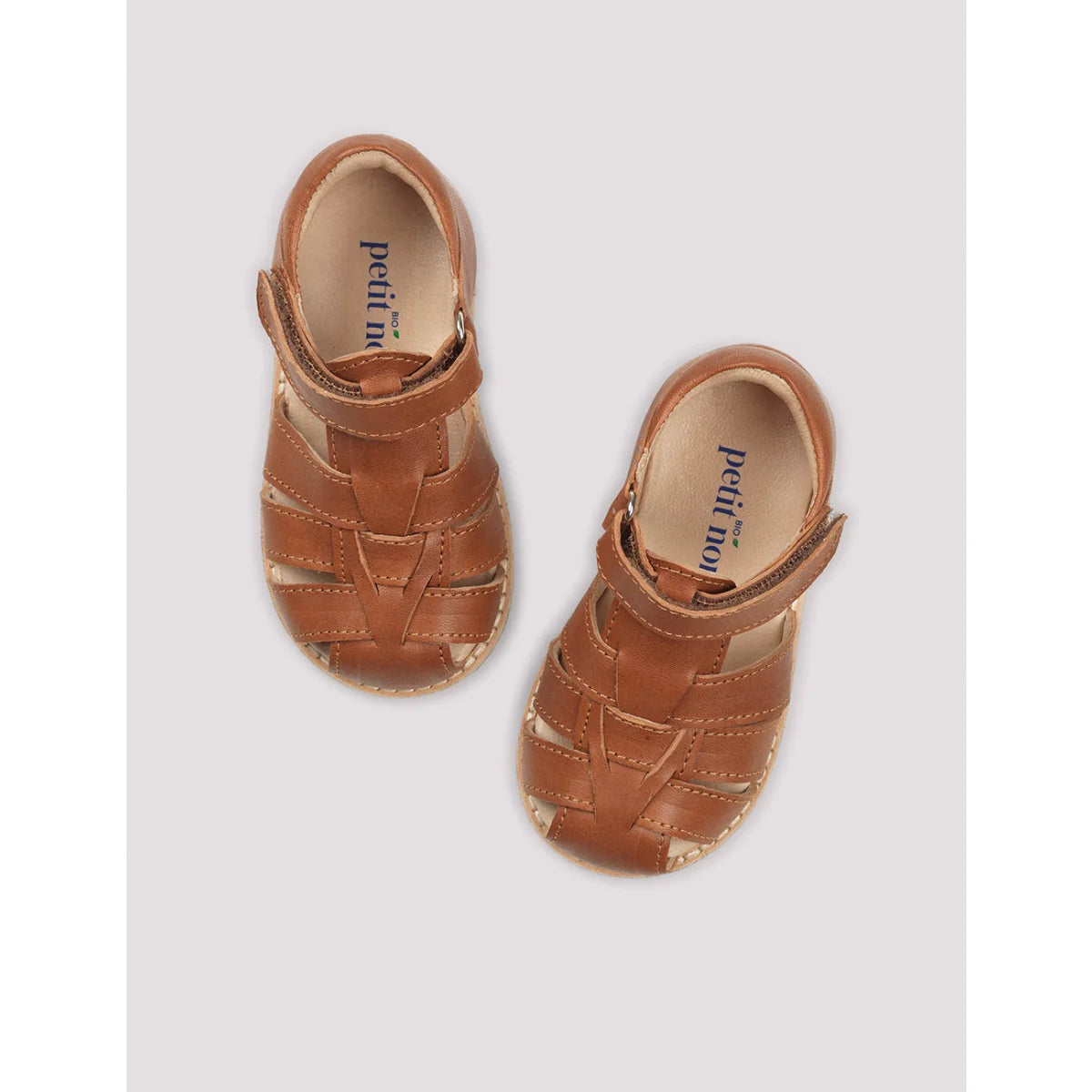 Klassische cognacfarbene baby sandalen aus tan leder mit gewebtem riemen und sichtbarem petit noir logo auf der innensohle