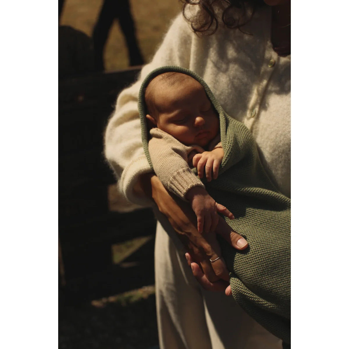 Neugeborenes Baby in grüner Decke, sanft in den Armen gehalten, Cocoon Babydecke Artischocke