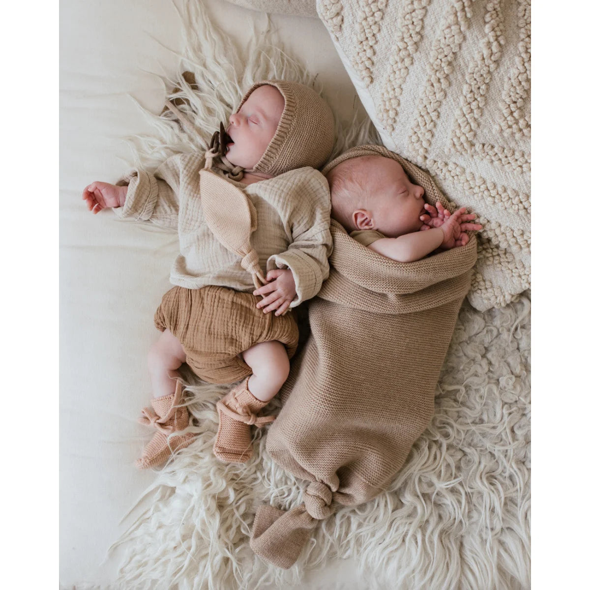 Neugeborenes Baby schläft friedlich in gemütlicher Strickkleidung auf Cocoon Babydecke Sand