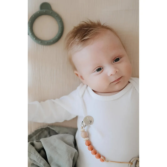 Baby in weißem Overall mit dekorativem Perlenanhänger, Fixleintuch Fog Nebel