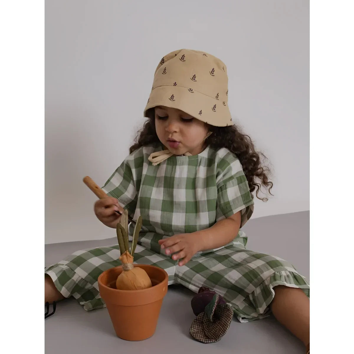 Kind mit beigem Eimerhut, Dill Gingham Frill Culottes auf dem Boden sitzend