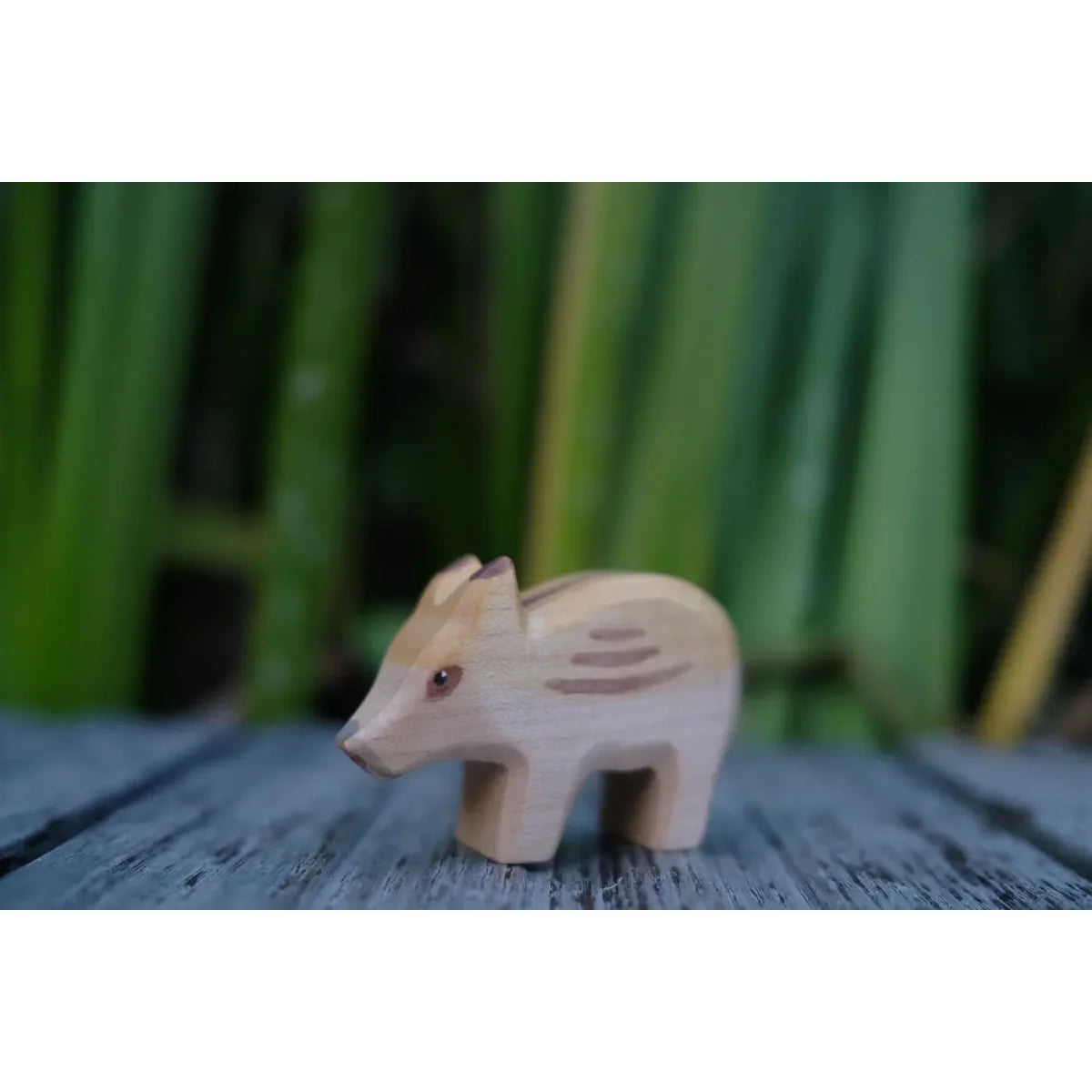 Helle Holzfigur eines Baby-Wildschweins mit braunen Streifen, namens Frischling