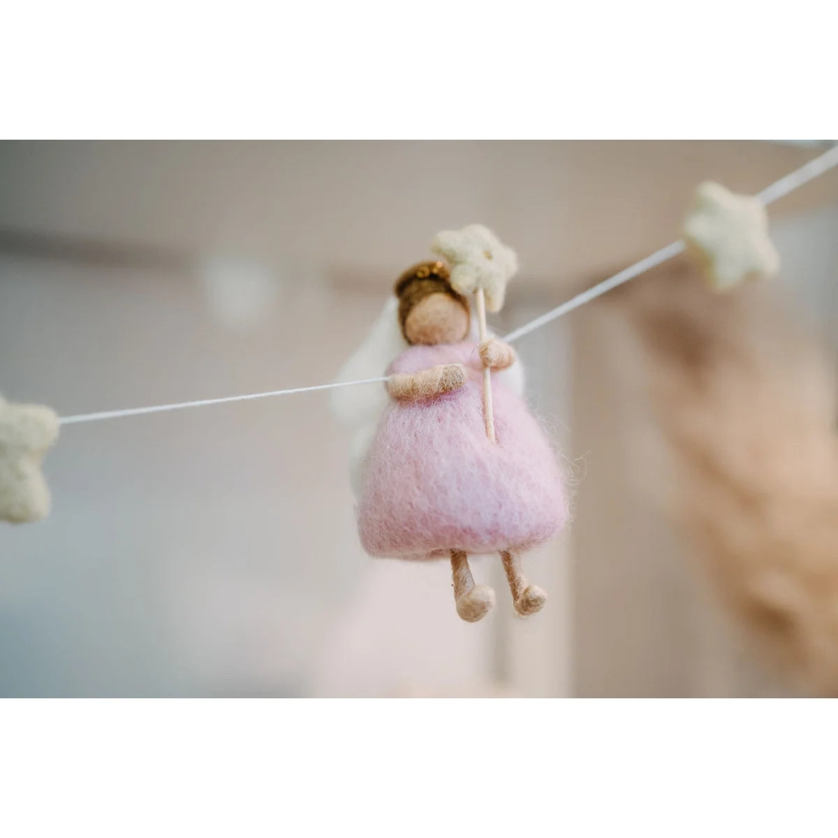 Eine weiche rosa filzengelornament mit weißem schleier und goldenem haar hängt an einer girlande feen und sterne