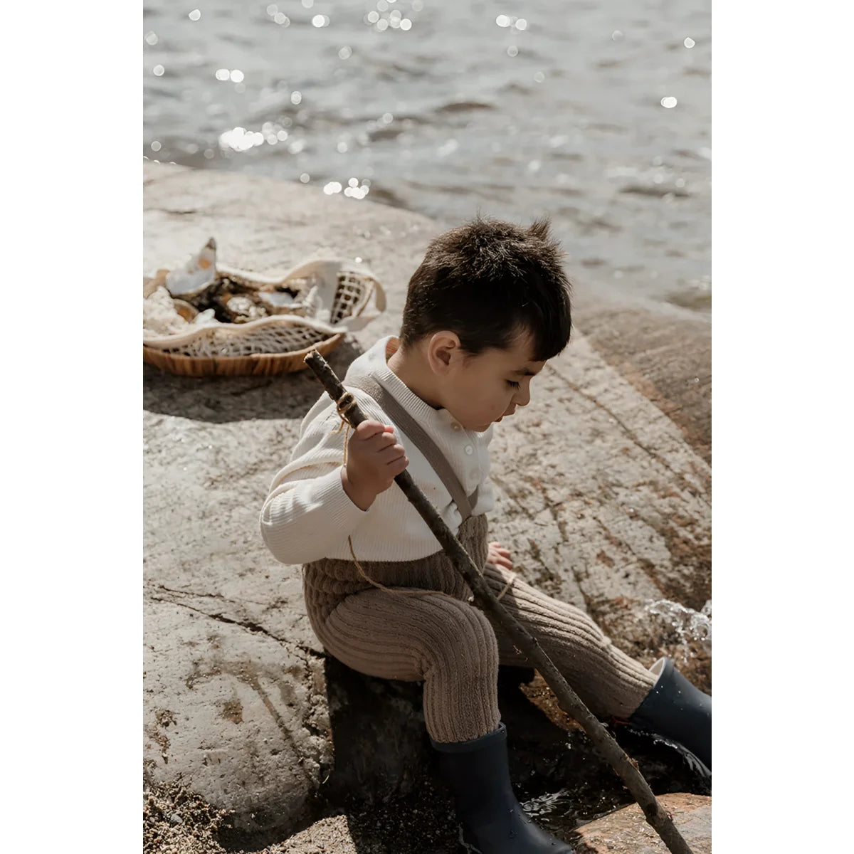 Junger Junge in Vintage-Kleidung sitzt auf Felsen am Wasser neben Granny Teddy Strumpfhosen