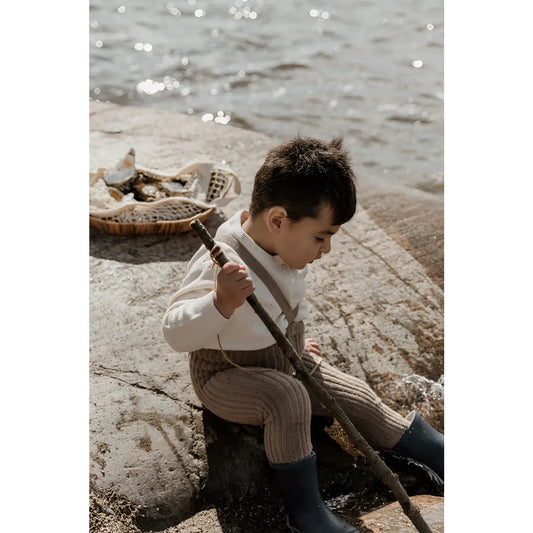 Junger Junge in Vintage-Kleidung sitzt auf Felsen am Wasser neben Granny Teddy Strumpfhosen
