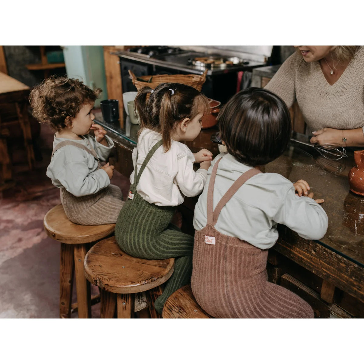 Drei Kinder auf Holzschemel am Tisch, tragen Granny Teddy Strumpfhosen in Peanut Blend