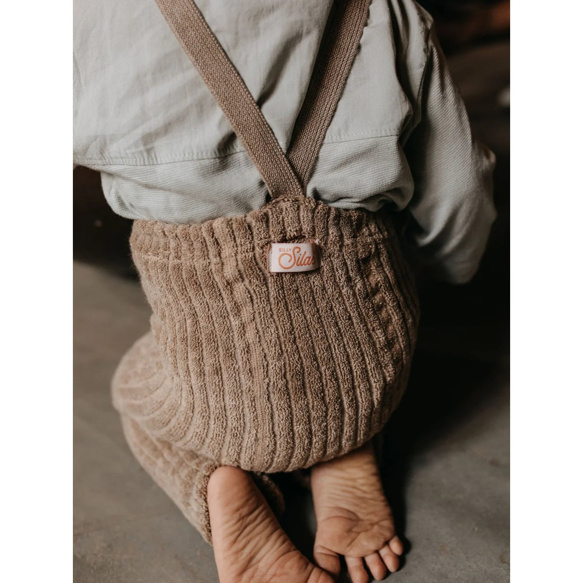 Beiger Corduroy Baby-Romper mit Trägern und sichtbaren nackten Füßen im Peanut Blend