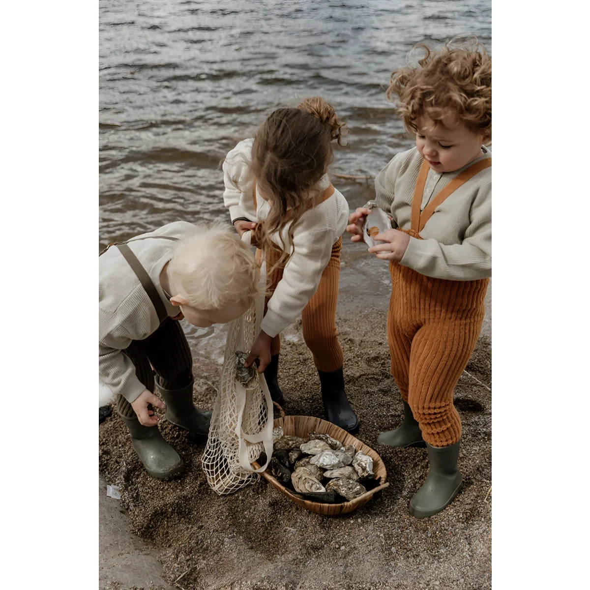 Drei Kinder erkunden eine felsige Küstenlinie und sammeln Gegenstände