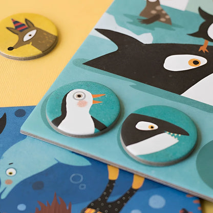 Runde Holzspielmarken mit Pinguin- und Haifisch-Motiven auf türkisem Grund für Habitats Lotto