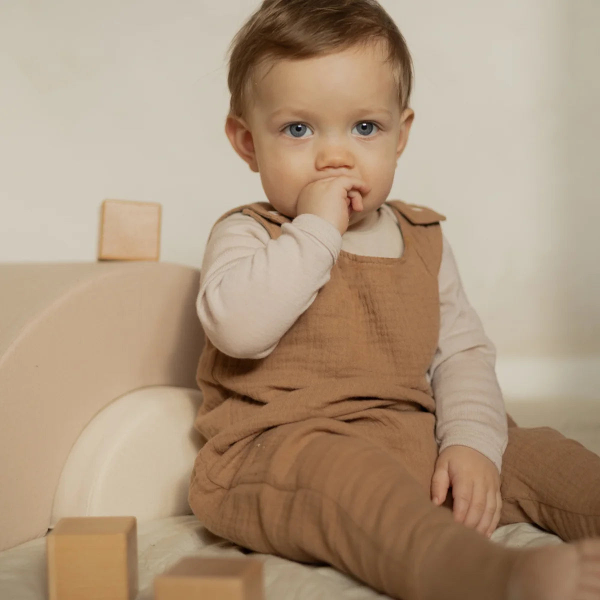 Baby in tan overalls outfit with white shirt, featured in Harem Romper beige