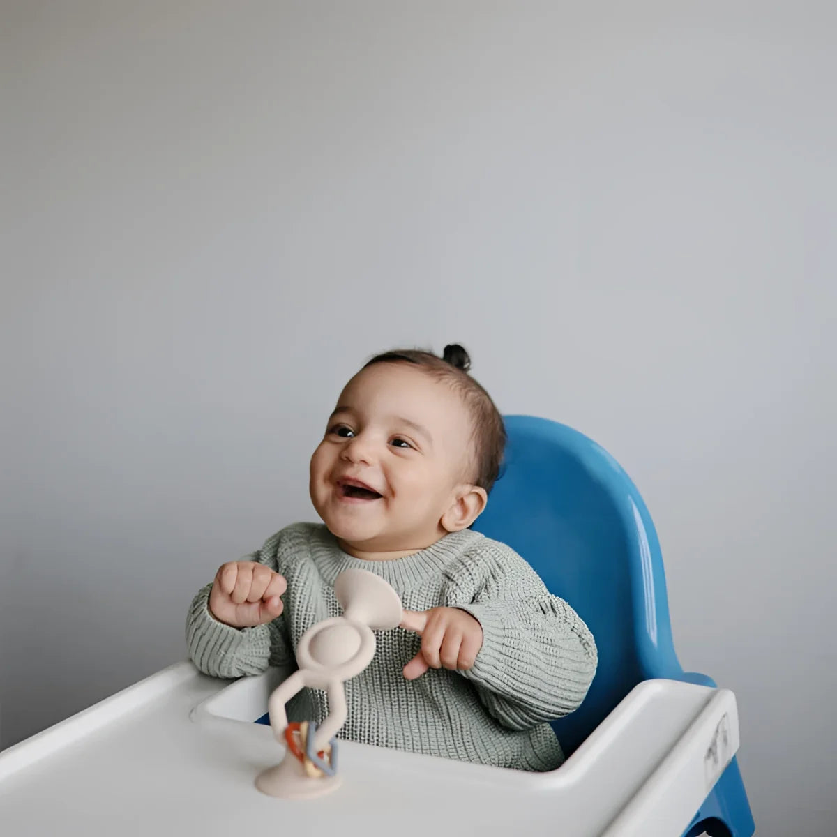 Lächelndes Baby sitzt im Hochstuhl mit HexaPop Saugnapf Spielzeug