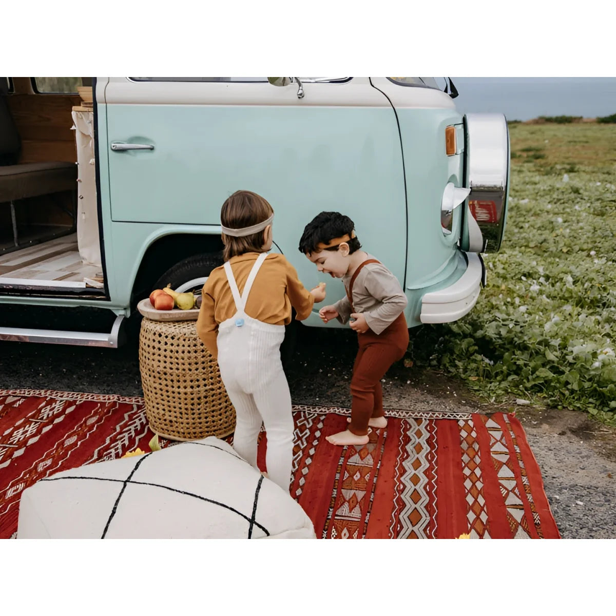 Zwei Kinder in Erdfarbenoutfits bei blau-weißem VW-Bus, mit Trägern und Zimt