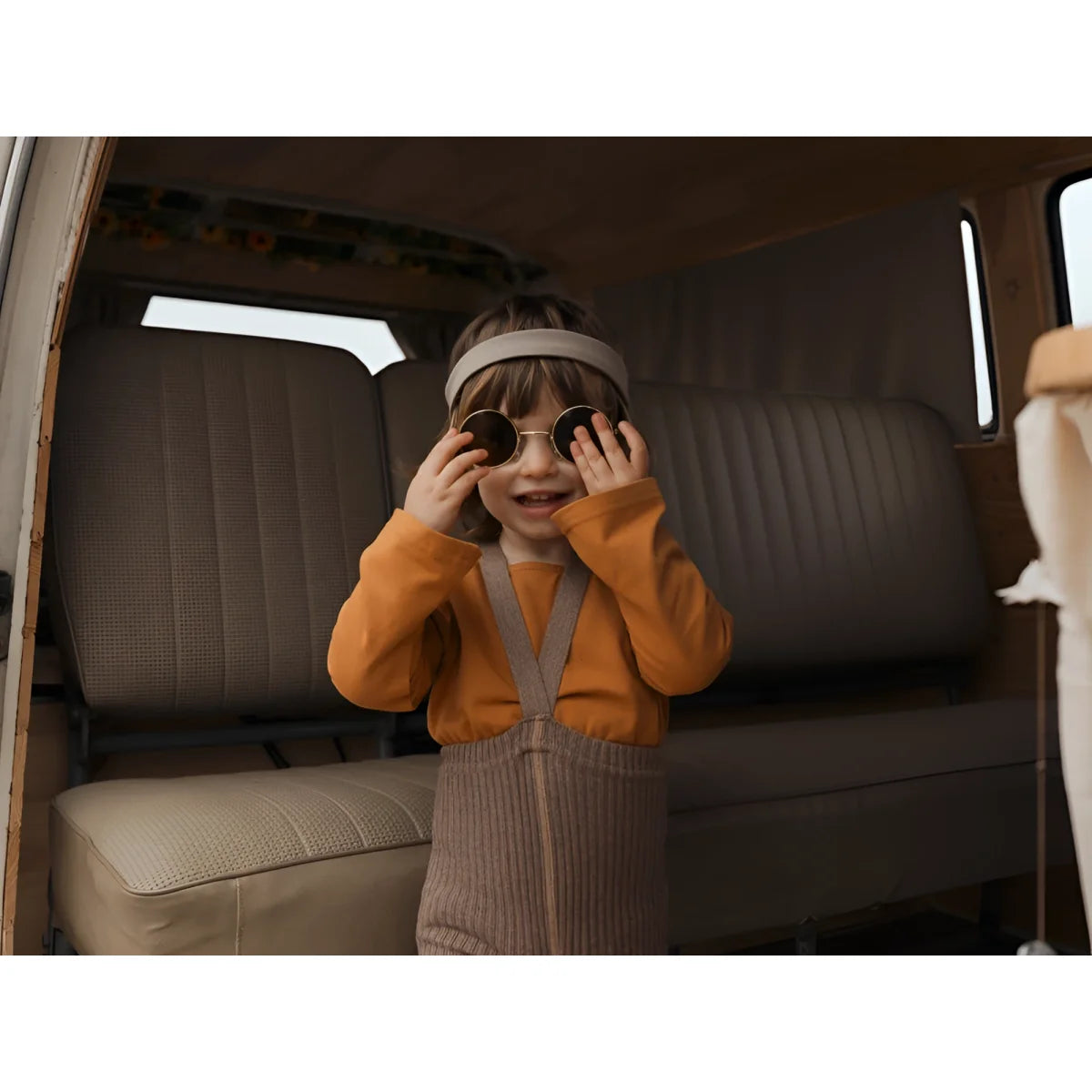 Kind mit orangefarbener Sweatshirt und beigen Hosen in Fahrzeug, Augen mit Händen verdeckt