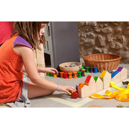 Ein kind in einem orange gepunkteten top spielt mit farbigen holzspulen und blöcken im spielset houses + nins