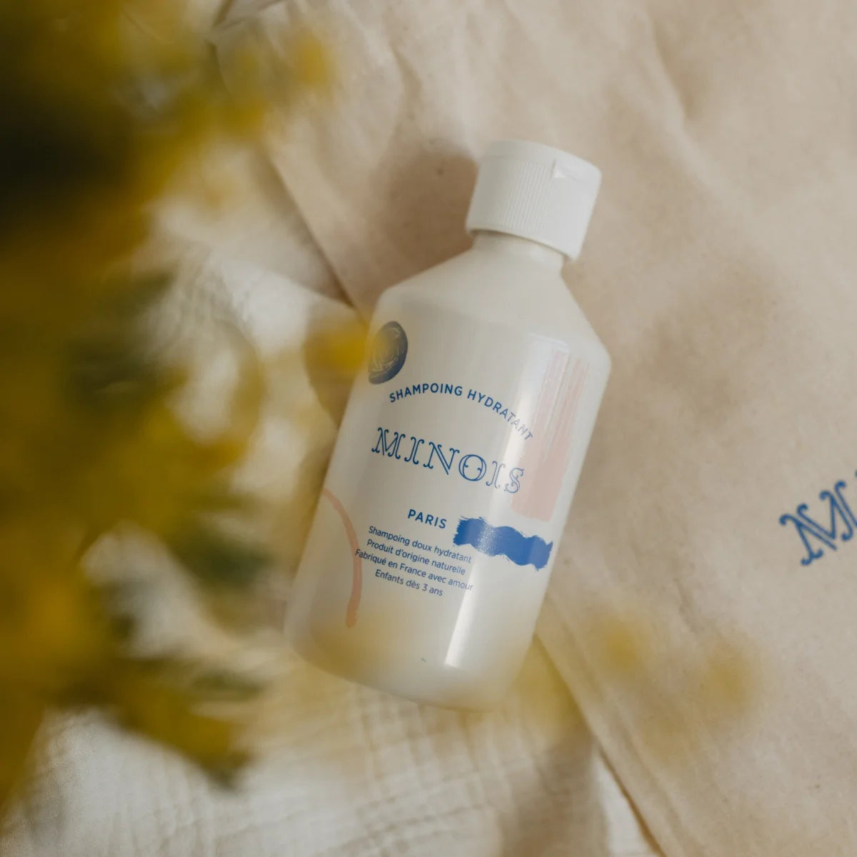 Eine weiße plastikflasche minois paris hydrating shampoo mit minimalistischem etikett in blau und rosa 300 ml