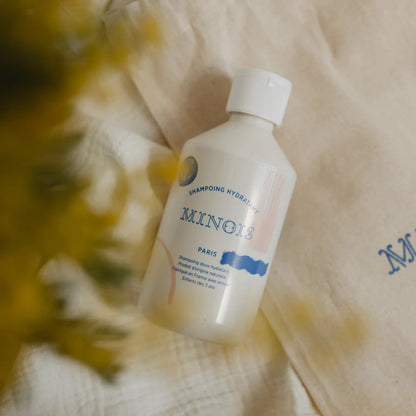 Eine weiße plastikflasche minois paris hydrating shampoo mit minimalistischem etikett in blau und rosa 300 ml
