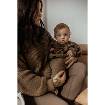Mutter, die ein Baby auf ihrem Schoß hält, trägt unregelmäßige Rippstrickleggings in Kaffee