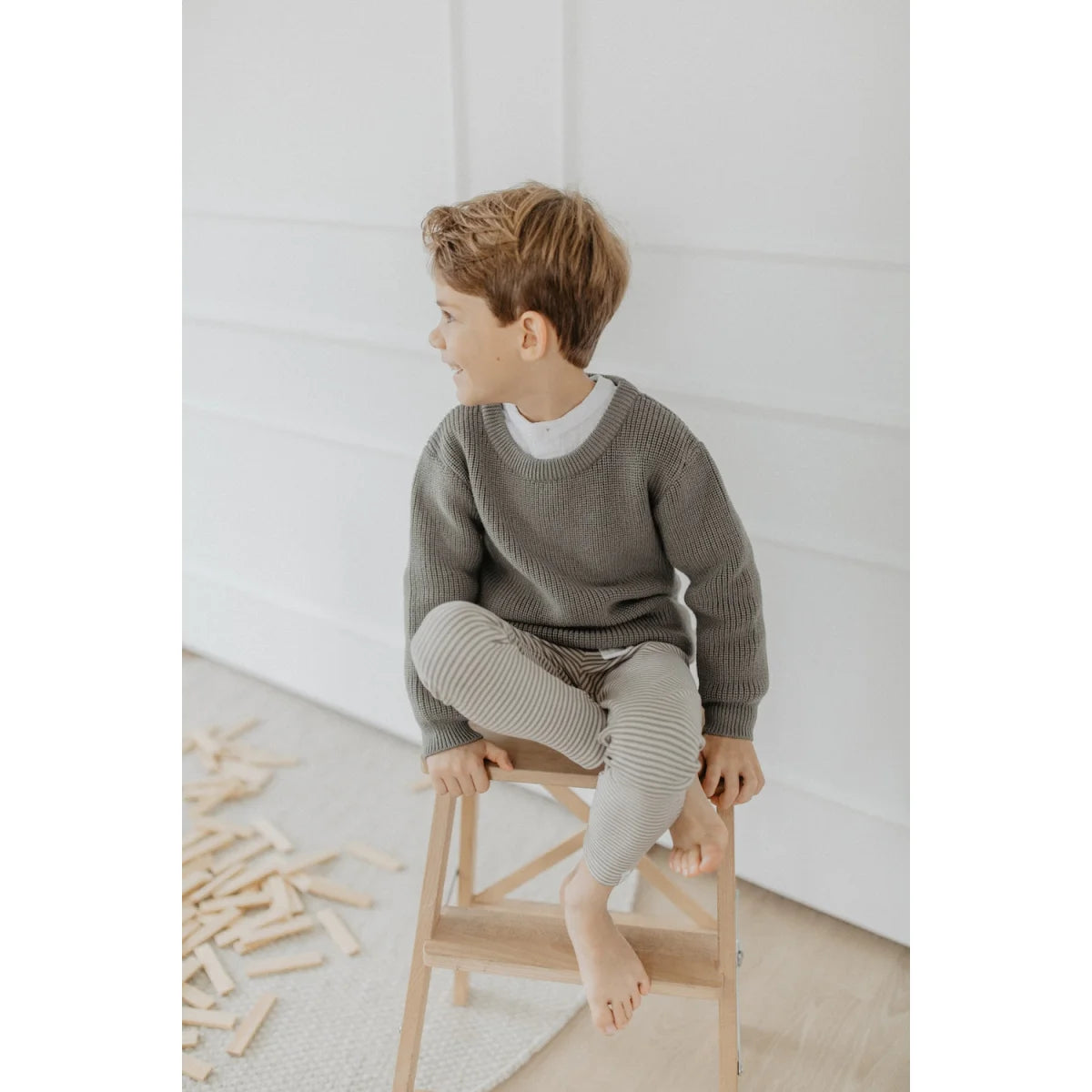 Junge in olivgrünem Strickpullover, weißem Shirt und Jersey-Leggings Grünstreifen