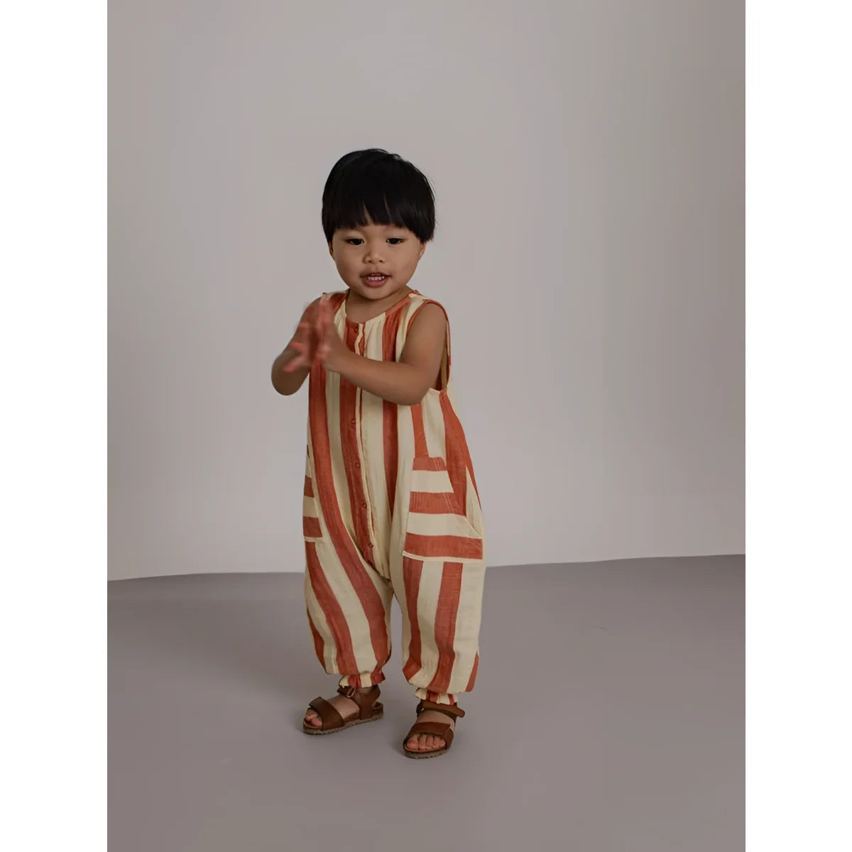 Kind in rückenfreiem Jumpsuit Tomato Stripes mit orange-cremefarbenen Streifen