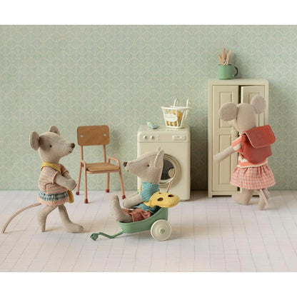Eine weiche beige mausfigur mit blauem pullover und brauner hose sitzt in einem mintgrünen spielzeugwagen kleine schwester