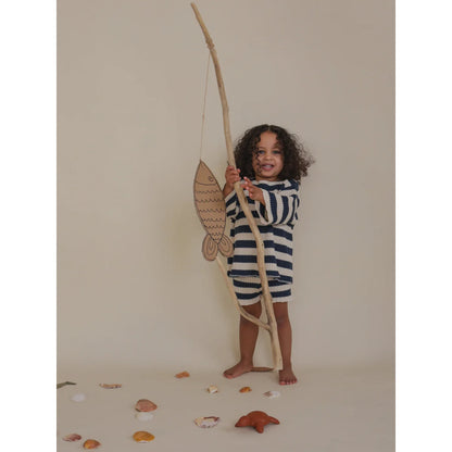 Kind mit Angelrute und Pappfisch trägt gestreifte Strickshorts