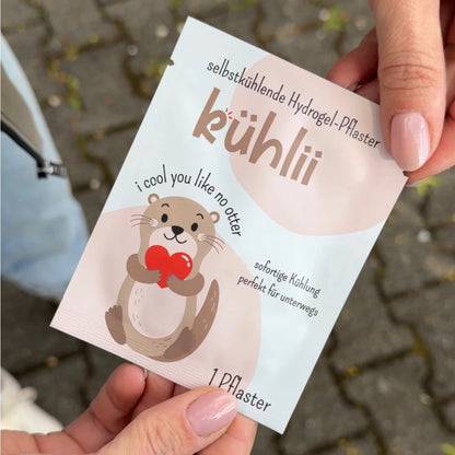 Ein süßer beige brauner cartoon-otter hält ein rotes herz auf einer weißen selbstkühlenden hydrogelpflaster-packung