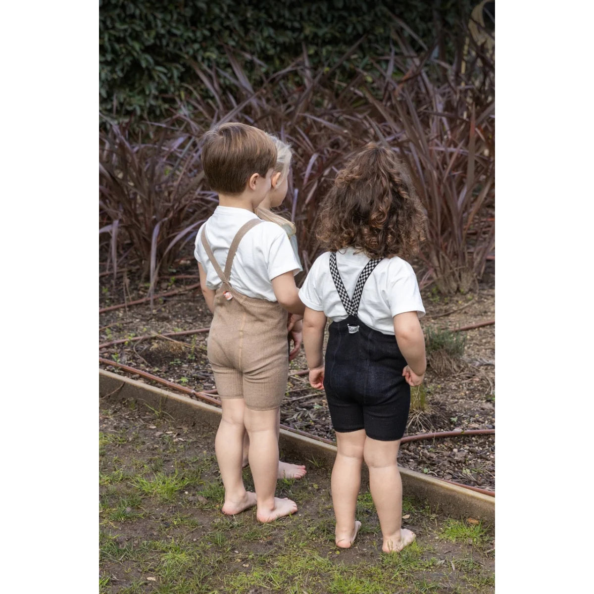 Drei Kinder in Hosenträger-Shorts mit klassisch schwarz-weißem Karomuster