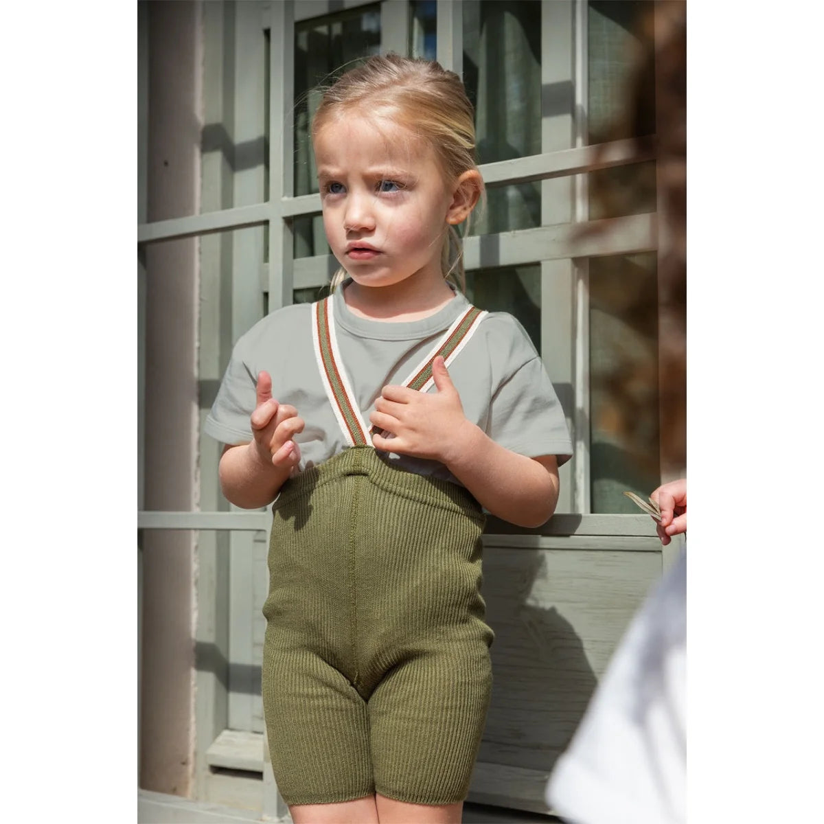 Kind in grünen Strickshorts und grauem Shirt mit Trägern für Kurze Strumpfhose
