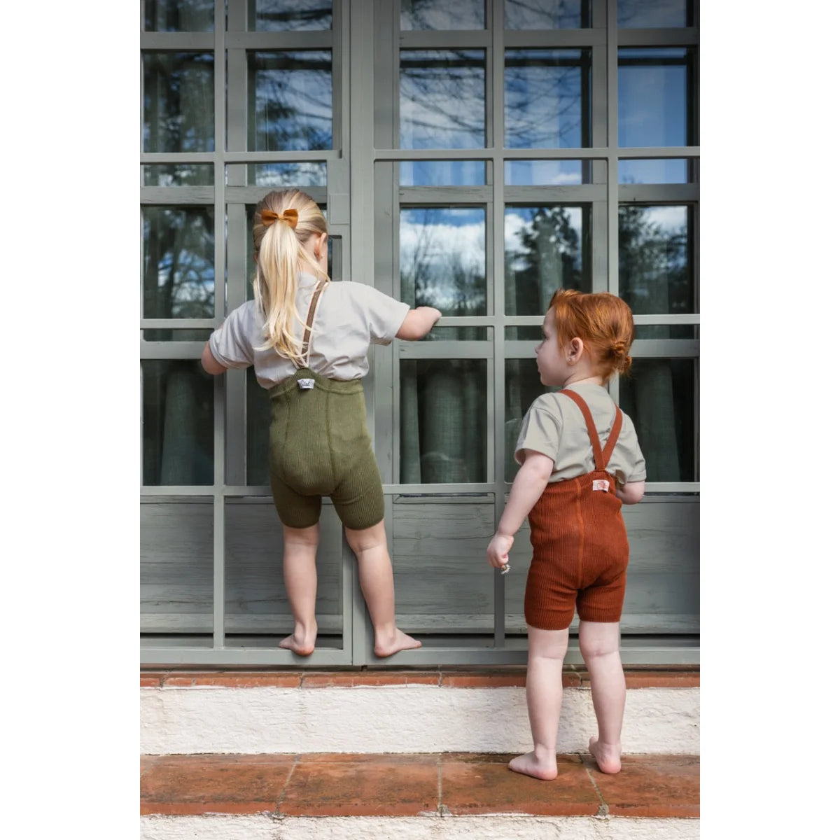 Zwei Kinder in Lederhosen, die kurze oliv gestreifte Strumpfhose mit Träger tragen