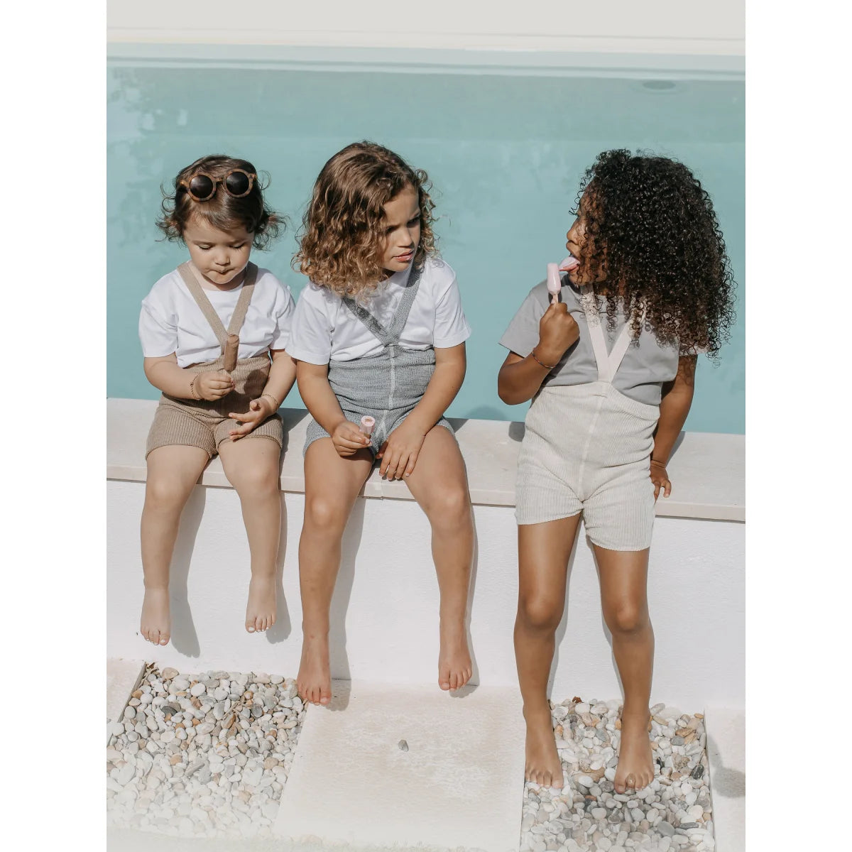 Drei Mädchen in weißen Shirts und hellen Shorts neben einem Pool mit Kurze Strumpfhose